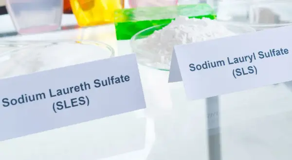 Białe proszki w naczyniach laboratoryjnych, jeden oznaczony jako Sodium Laureth Sulfate (SLES), drugi jako Sodium Lauryl Sulfate (SLS).