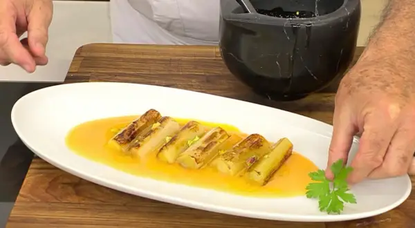 Puerros a la plancha, dorados y tiernos, bañados en una salsa dorada y decorados con perejil fresco.