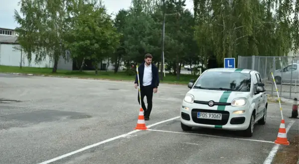 Młody mężczyzna ustawia pachołek na placu manewrowym, przygotowując się do egzaminu praktycznego.