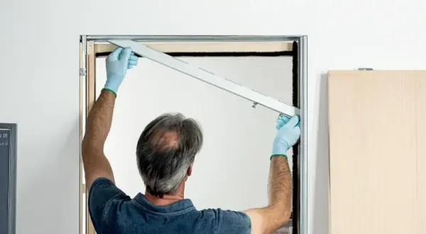 Installazione controtelaio porta scorrevole in cartongesso. L'operaio con guanti azzurri posiziona la guida superiore.