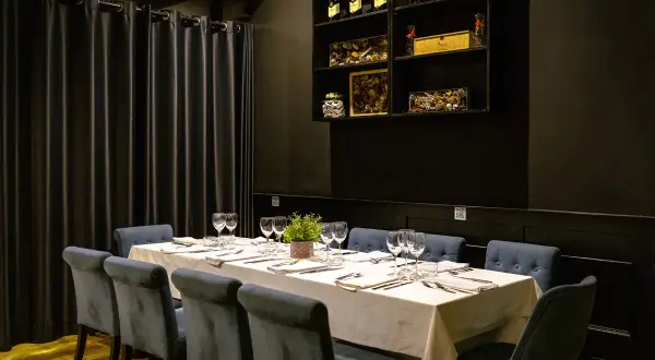 Mesa elegante con sillas azules y mantel blanco, lista para el menú del día de la buganvilla. Botellas de vino en estantería.