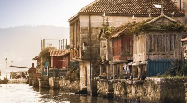 Casas de piedra y madera junto al agua, gaviotas en los tejados. Un ejemplo de los pueblos bonitos de Galicia.