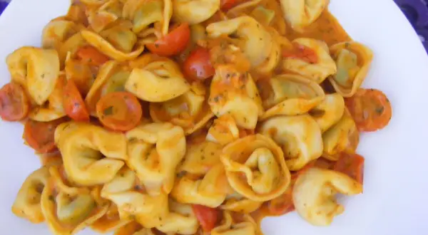 Pyszne tortellini ze szpinakiem w kremowym sosie pomidorowym z kawałkami pomidorków.
