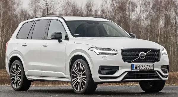 Białe Volvo XC90 T6 z czarnymi felgami stoi na drodze, za nim las.