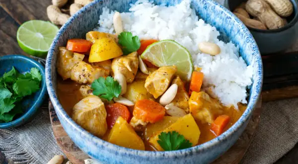 Ein köstlicher Massaman Curry mit Hühnchen, Kartoffeln, Karotten und Erdnüssen, serviert mit Reis und Limettenspalten.