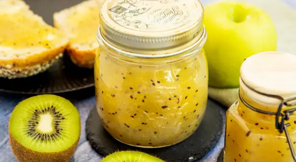 Ein Glas hausgemachte Kiwi-Marmelade mit frischen Kiwis und Toast.
