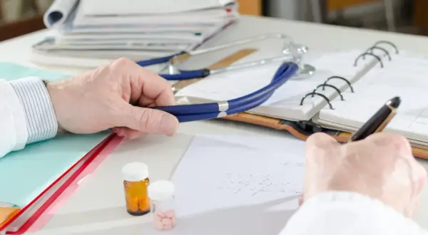 Lekarz pisze receptę, obok stetoskop i leki. Czy do dermatologa na NFZ trzeba mieć skierowanie?