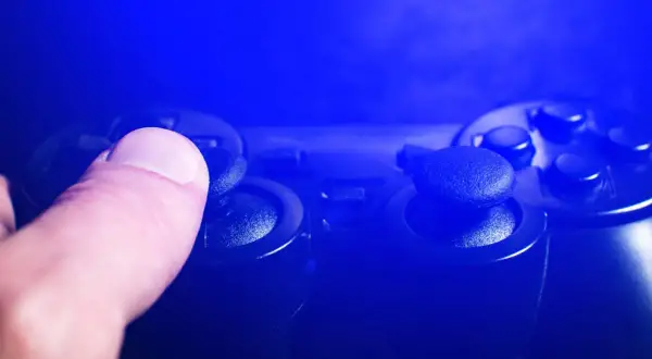 Dłoń naciska joystick kontrolera do gier w niebieskim świetle.