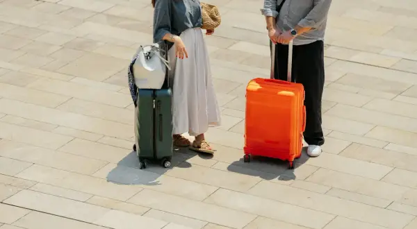 Para podróżnych z bagażami, w tym zielona podręczna walizka na kółkach Wizzair, gotowa na wakacje.