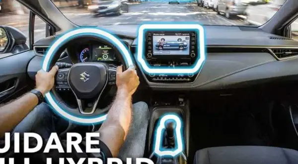 Interno di un'auto ibrida, con le mani sul volante e il display centrale acceso. Scopri il significato di auto ibrida e guida in modo ecologico.