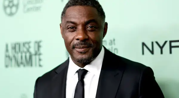 Idris Elba, znany z filmów, seriali i programów, w czarnym garniturze i krawacie.