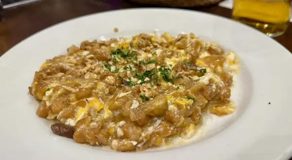 Delicioso revuelto de bacalao con trocitos de frutos secos y perejil picado, servido en un plato blanco.