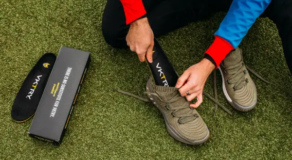 Un homme change la semelle intérieure de sa chaussure de sport sur un terrain artificiel.