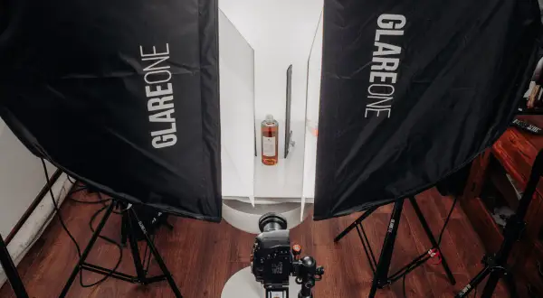 Profesjonalna fotografia produktowa jak zacząć? Zestaw oświetleniowy z dwiema lampami Glareone, aparatem i butelką w tle.