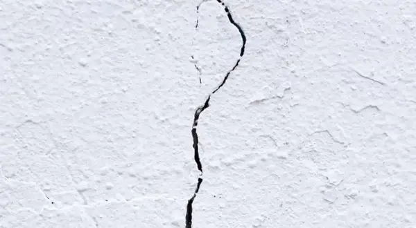 Una pared blanca con textura rugosa muestra grietas por dilatación, una línea oscura que se abre paso a través de la superficie.
