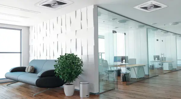 Un moderno ufficio con un divano, una pianta e un condizionatore incassato nel controsoffitto. La zona lavoro è separata da pareti in vetro.