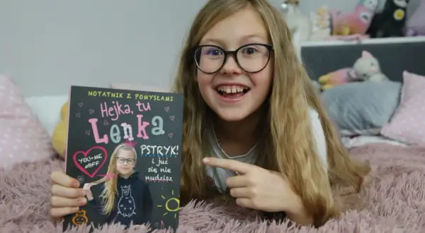 Hejka, tu Lenka! Dziewczynka z okularami trzyma notatnik z napisem "Hejka, tu Lenka".