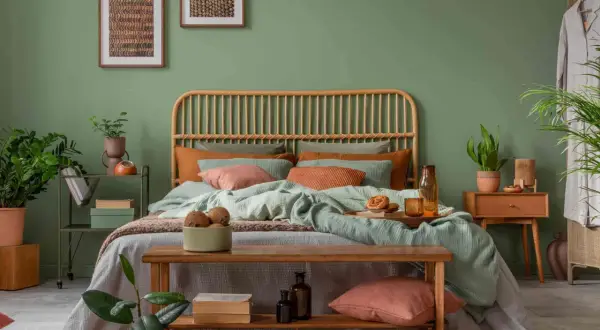 Gemütliches Schlafzimmer mit Rattan-Kopfteil, mintgrüner Bettwäsche und Korallen-Akzenten. Ein Holzbett mit Kissen und Decken lädt zum Entspannen ein. Pflanzen und Bilder runden das Ambiente ab, um das Bett perfekt einzurichten.