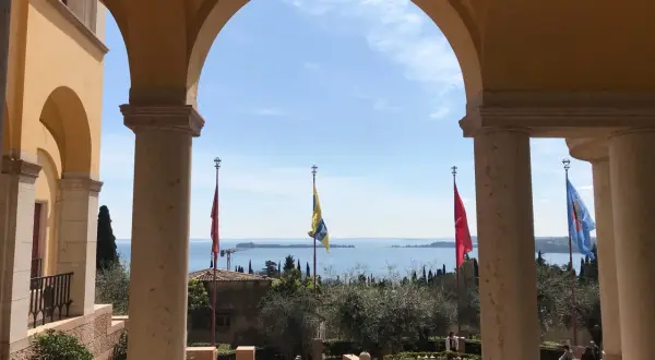Arco con vista sul lago, giardini e bandiere che sventolano, ricordando l'atmosfera della villa d'Annunzio.