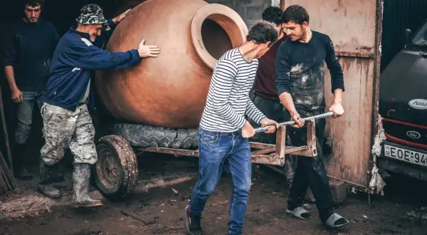 Mężczyźni przenoszą wielką glinianą qvevri, tradycyjny gruziński pojemnik do produkcji win.
