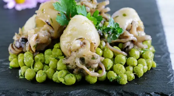 Delizioso piatto di seppie con piselli, guarnito con prezzemolo e erbe aromatiche, servito su una pietra scura.