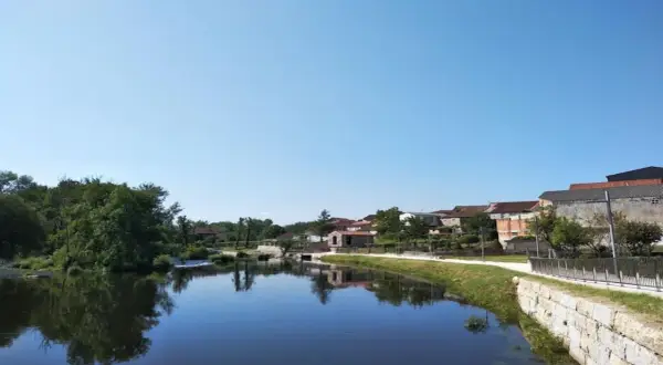 Tranquila playa fluvial en Leiro, con casas tradicionales reflejándose en el agua serena bajo un cielo azul.