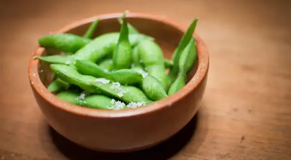 Miseczka pełna zielonej fasolki edamame posypanej solą, gotowa do chrupania.