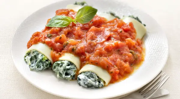 Cannelloni ricotta épinard généreusement nappés de sauce tomate, garni d'une feuille de basilic. Un plat savoureux et réconfortant.