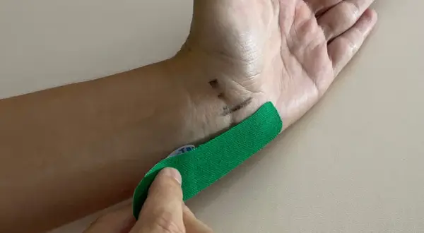 Hand mit grünen Tape, das auf das Handgelenk geklebt wird, um Taubheitsgefühl im kleinen Finger zu lindern.
