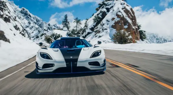 Biały Koenigsegg Agera z czarnym pasem pędzi po ośnieżonej górskiej drodze.