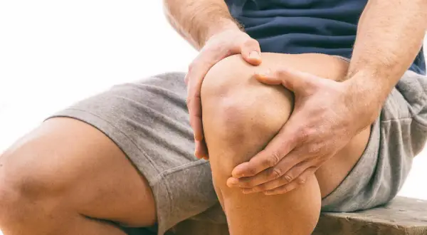 Uomo con dolore al ginocchio, mani che stringono l'articolazione. Possibile problema al menisco, consulta un osteopata.