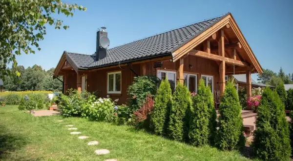 Drewniany domek w **wiosce wakacyjnej Radawa** otoczony zielenią. Kamienna ścieżka prowadzi do wejścia.