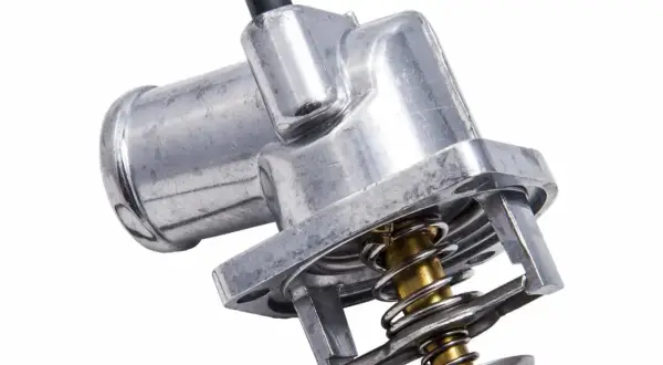 Metalowy termostat w samochodzie z widocznym mechanizmem sprężynowym i czarną złączką.