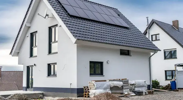 Nowy dom z panelami słonecznymi na dachu, w trakcie rozbudowy. Wokół materiały budowlane.