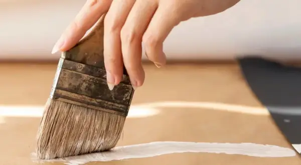 Main d'une personne peignant une surface en MDF avec un pinceau blanc.