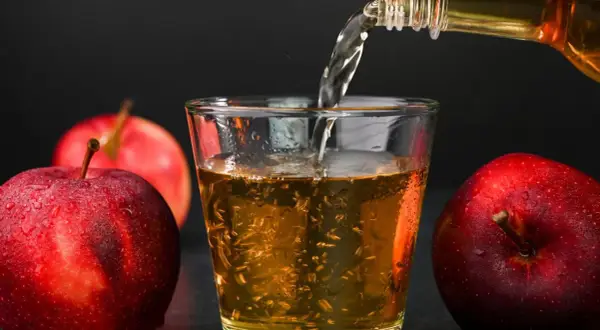 Apfelwein wird in ein Glas gegossen, umgeben von frischen Äpfeln. Ein gesunder Genuss!