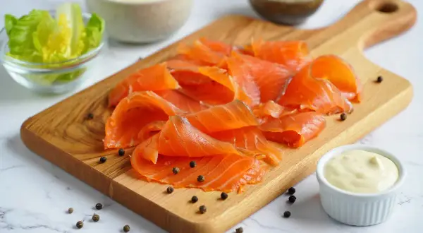 Deliciosa ensalada de salmón lista para preparar. Salmón ahumado en tabla de madera, lechuga, crutones, queso rallado y aderezo.