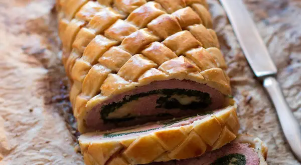 Un delizioso polpettone in crosta, con un ripieno di carne, spinaci e formaggio, pronto per essere affettato.