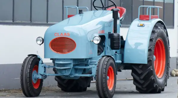 Niebieski ciągnik jednoosiowy Claas Jumbo z pomarańczowymi felgami i grillem.