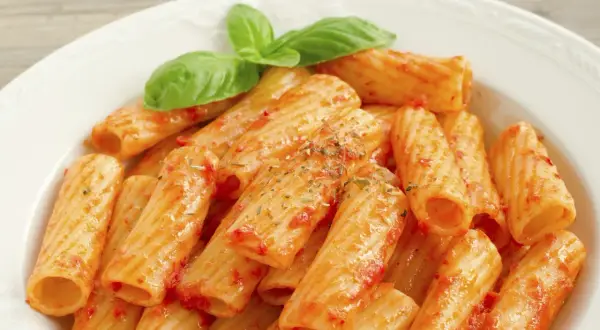 Un piatto di rigatoni al sugo, conditi con erbe aromatiche e guarniti con foglie di basilico fresco. Il maccarone, nella sua semplicità, racchiude un significato di convivialità e tradizione.