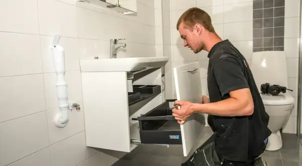 En man installerar en vit kommod i ett kaklat badrum.