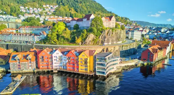 Kolorowe domy nad wodą w Bergen, idealne na wycieczki do Norwegii. W tle zielone wzgórza i zabudowania.