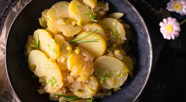 Schüssel mit Kartoffelsalat ohne Mayo, garniert mit Schnittlauch und Gurkenstückchen.
