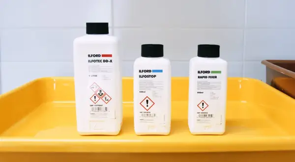Three Ilford bottles for developing, stopping, and fixing film sit in a yellow tray, ready for creating the best black and white film.