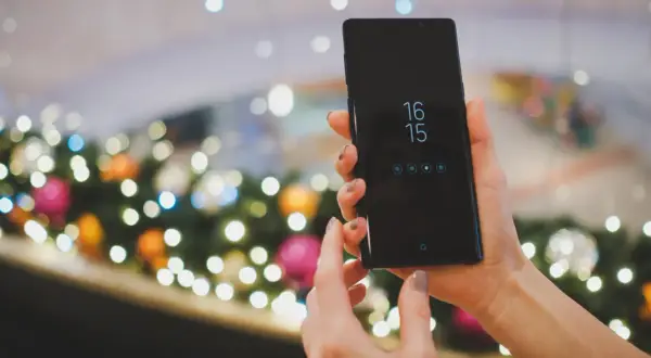Ręce trzymające czarny smartfon Samsung, na ekranie zegar i ikony. Planowane zgranie kontaktów z Samsunga na komputer.