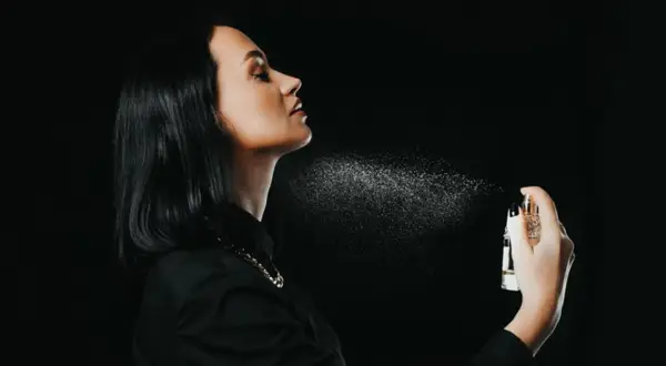 Kobieta rozpyla perfumy na szyję, tworząc mgiełkę zapachu. To idealne miejsce, gdzie psikac perfumami, by subtelnie podkreślić swoją obecność.