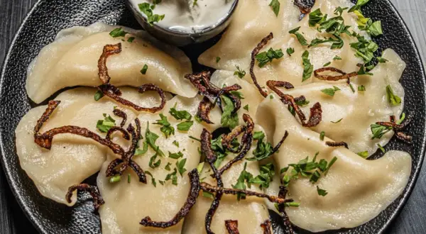 Pyszne pierogi z ziemniakami i boczkiem, posypane chrupiącą cebulką i natką pietruszki. Idealne z kwaśną śmietaną.