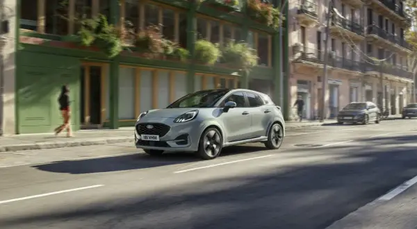 Jasnoszary Ford Puma jedzie ulicą miasta. Sprawdź aktualną ford puma cena i możliwości tego stylowego SUV-a.