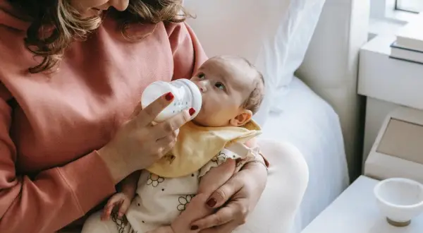 Mama karmi butelką dziecko, które ma problem z brakiem pokarmu po porodzie.