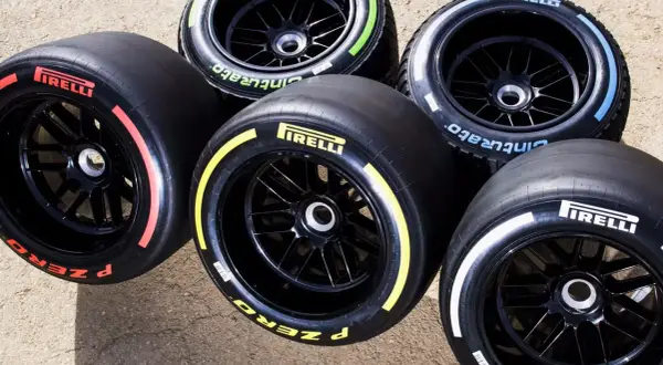 Pięć opon F1 Pirelli P Zero z kolorowymi paskami: czerwonym, żółtym, białym, zielonym i niebieskim, gotowych na wyścig.